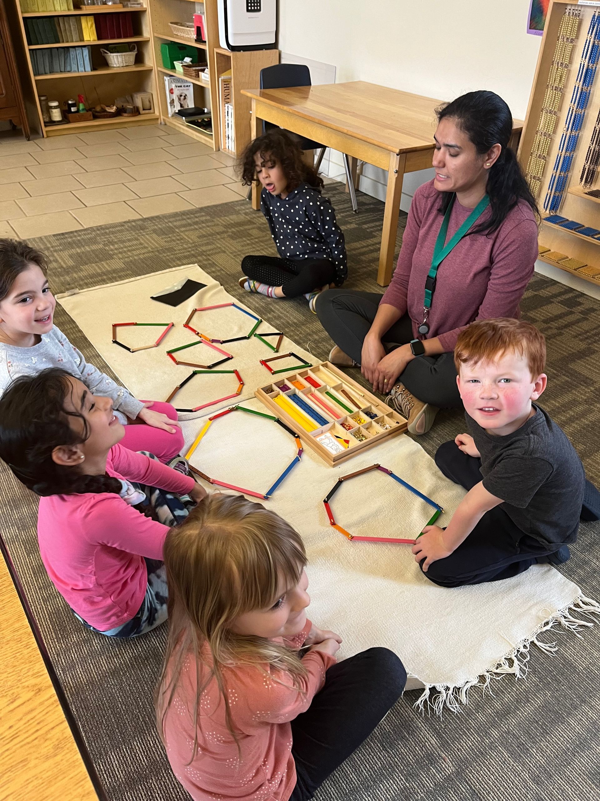 A group of children are sitting on the floor with a montessori guide.