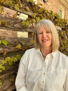 A woman in a white shirt is standing in front of a wooden fence.