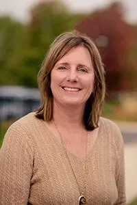 A woman in a brown sweater and necklace is smiling for the camera.