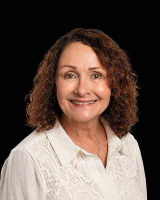 A woman in a white shirt is standing in front of a wooden fence.