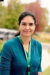 A woman in a blue shirt and green lanyard is smiling for the camera.