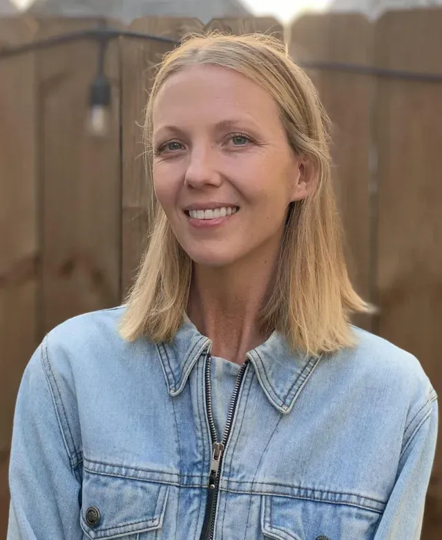 A woman in a denim jacket is smiling for the camera.