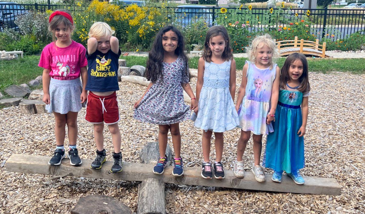 A group of children are standing on a log in a park.