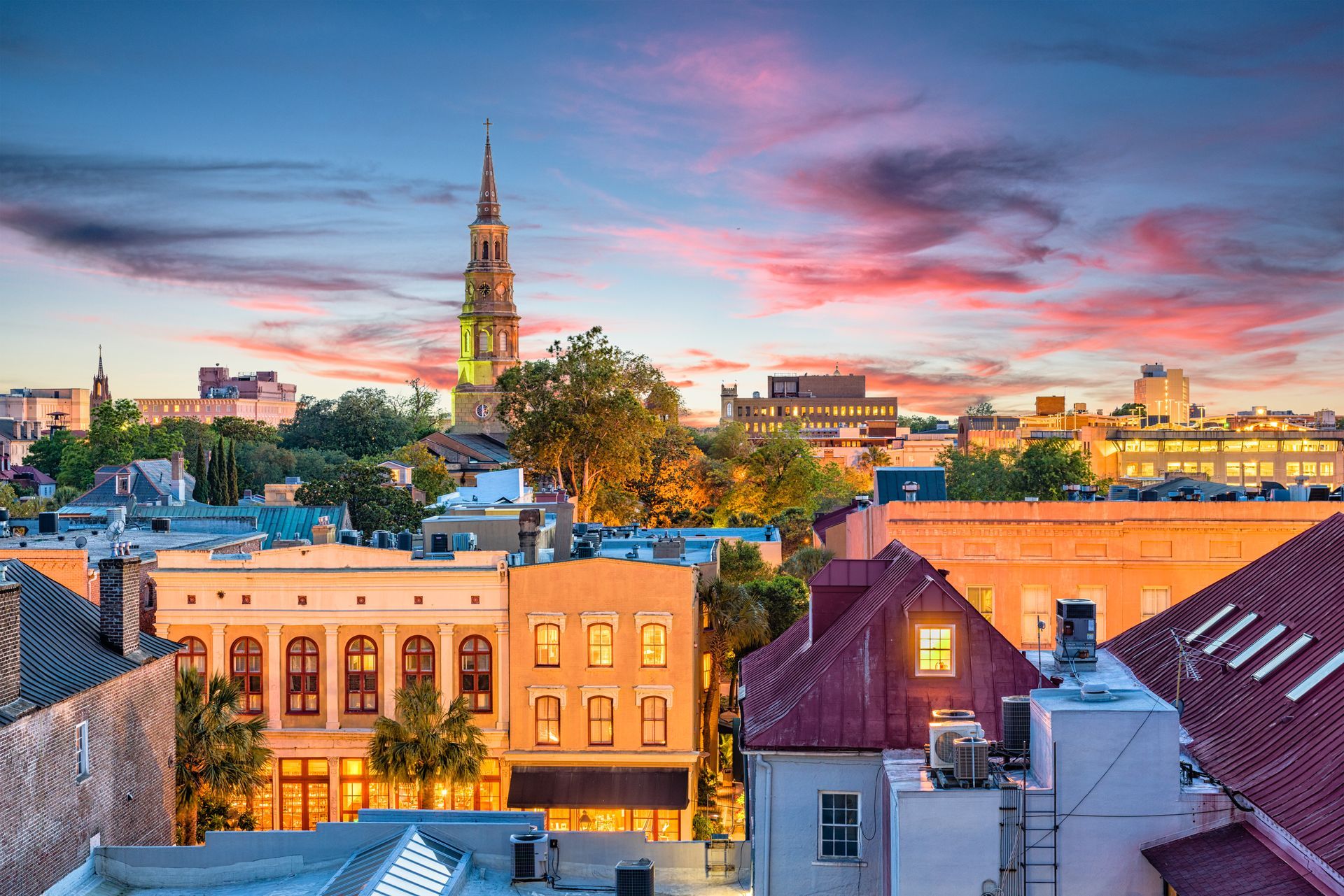 Charleston, South Carolina skyline at sunset with buildings and church steeple. Pink and purple sky.