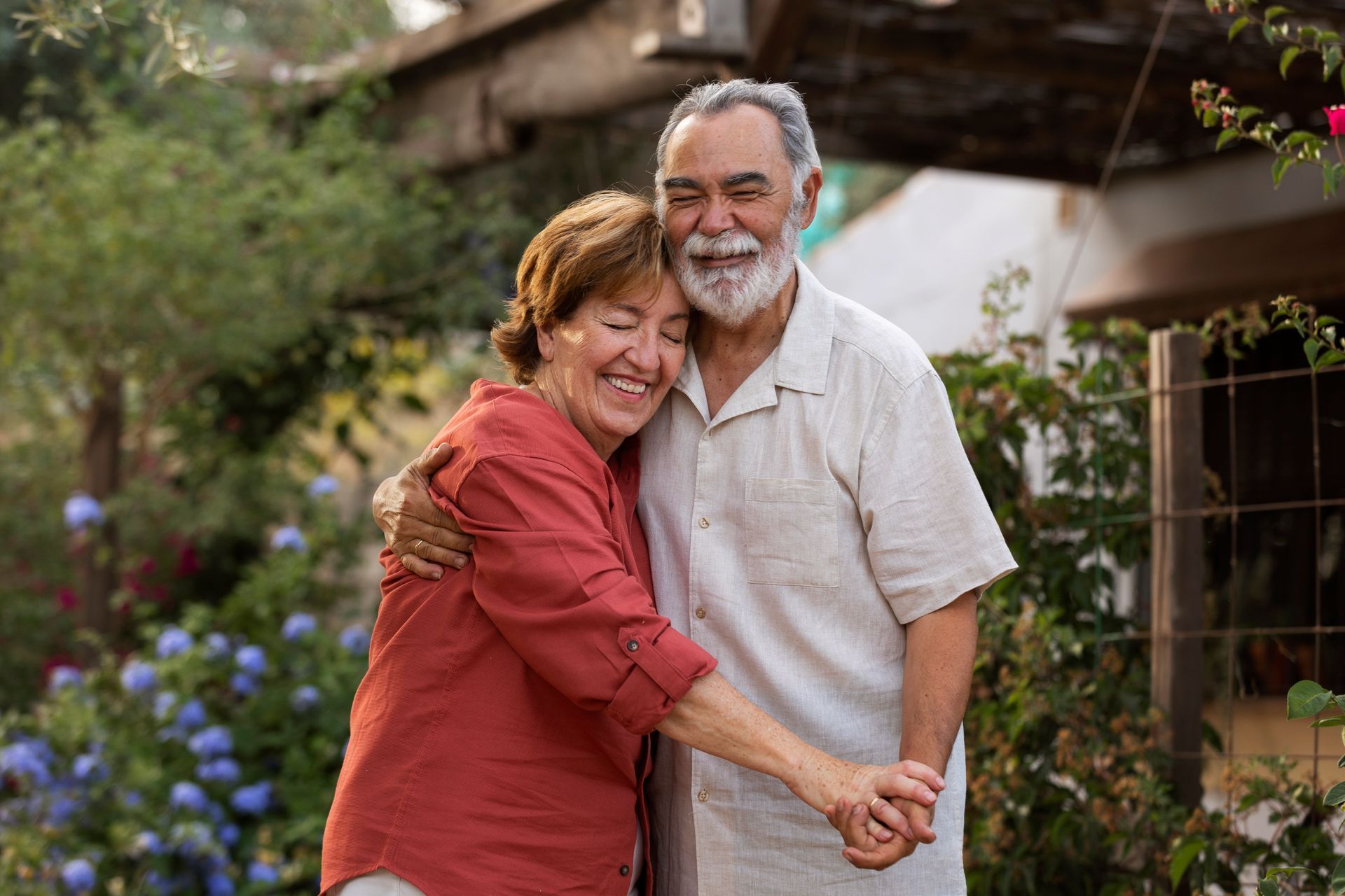 Smiling couple embracing outdoors, holding hands, in a garden.