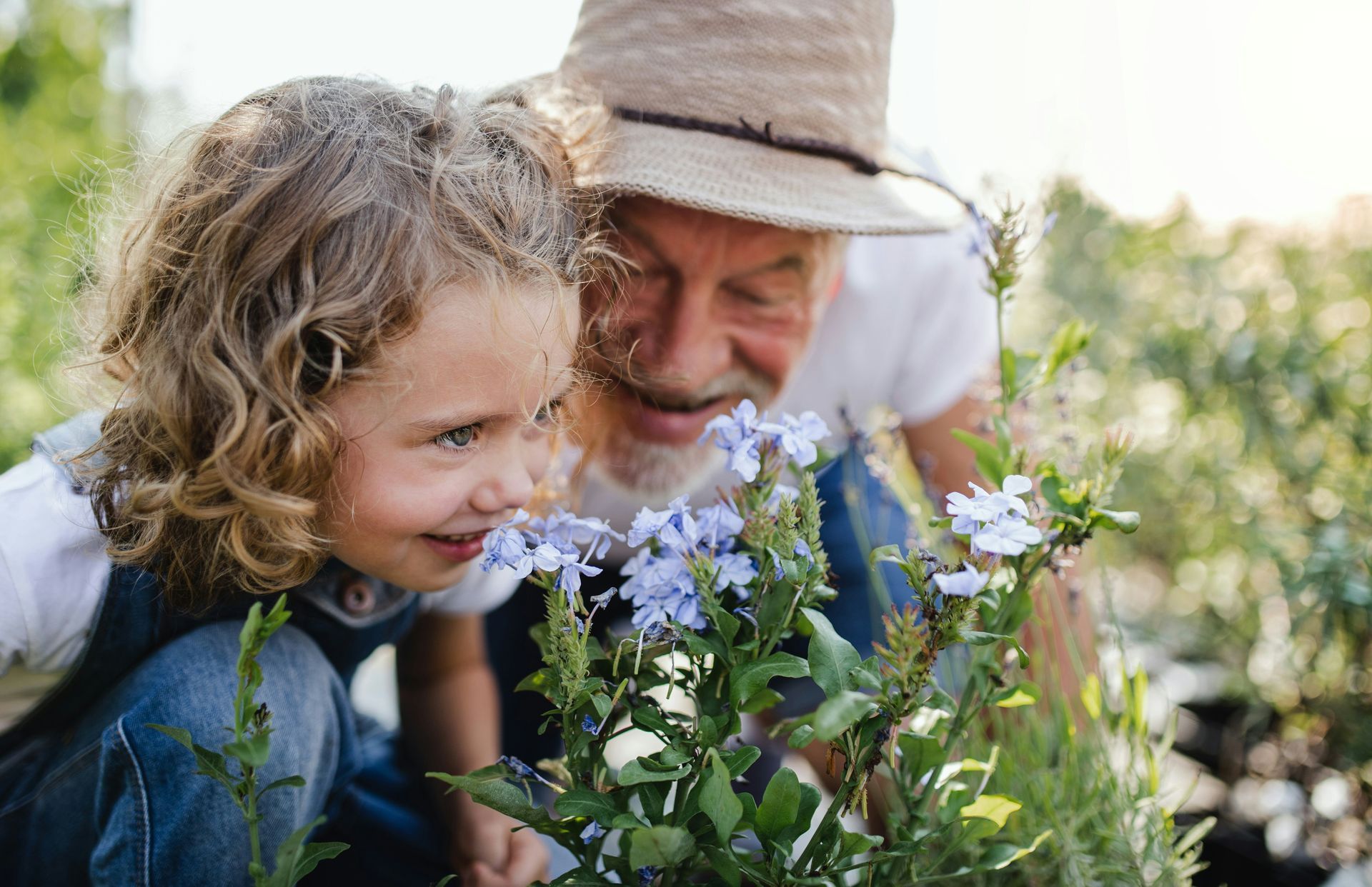 Child and older person smelling blue flowers in a garden.
