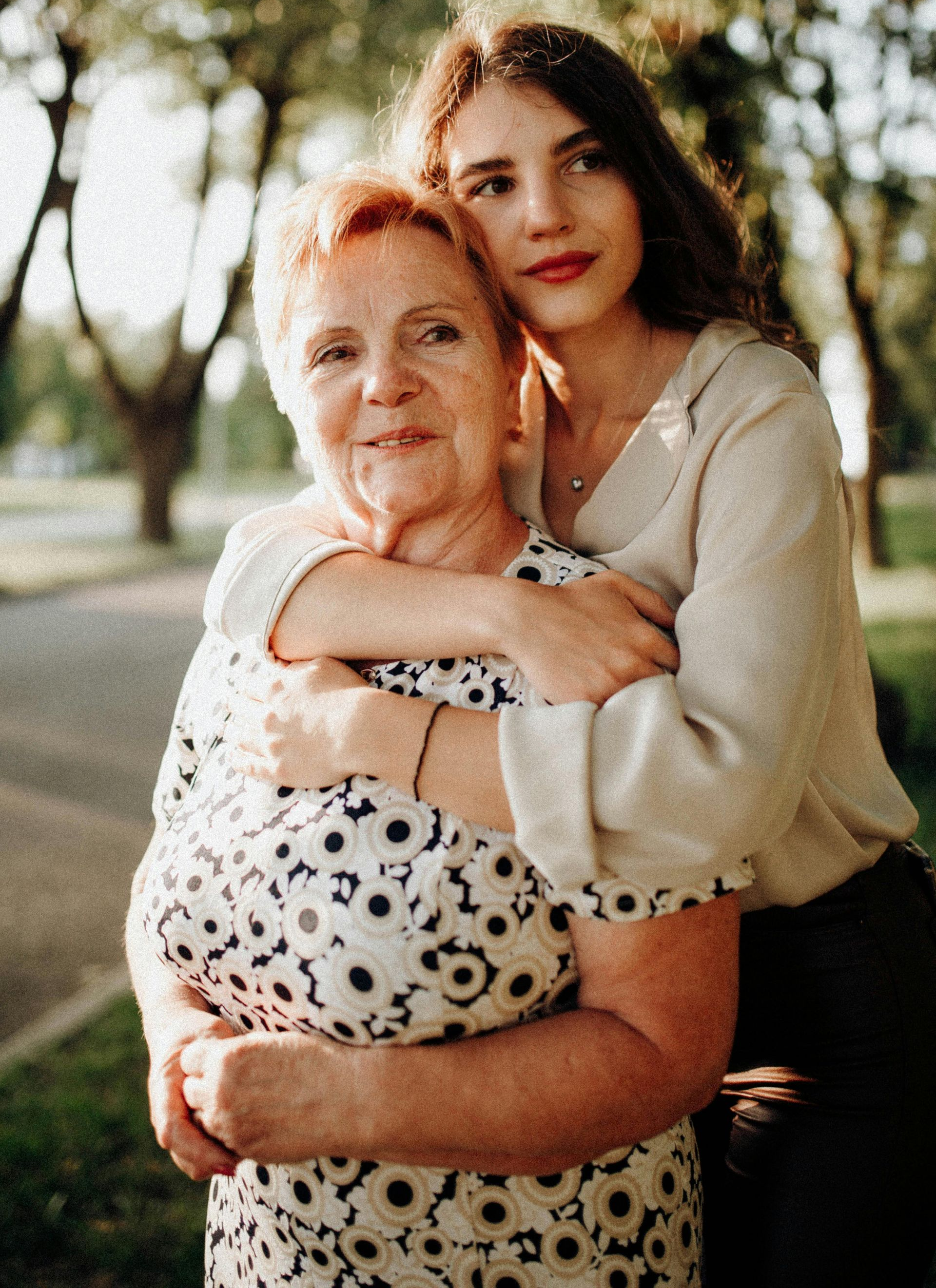 Woman embracing older woman outdoors, smiling.