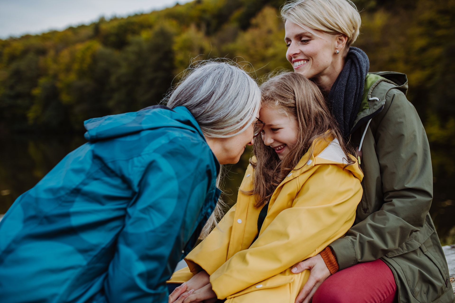 Three people, a child and two adults, smiling and embracing outdoors.