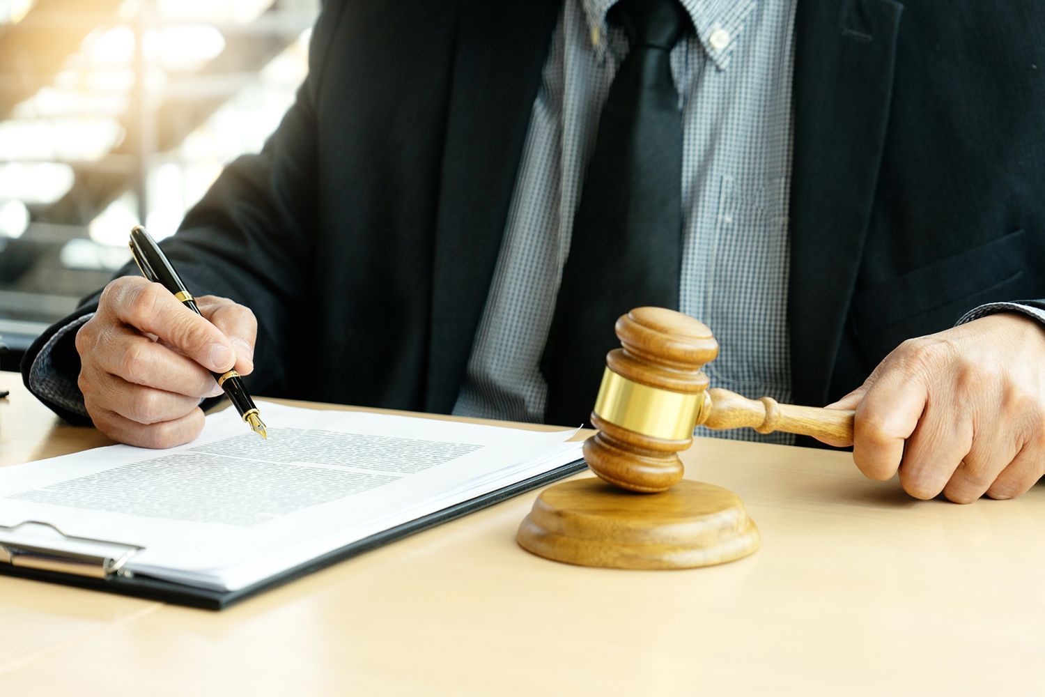 A man is sitting at a table holding a wooden gavel and writing on a clipboard.