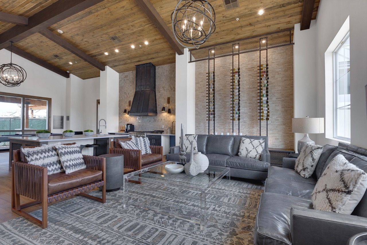 Indoor community lounge with sofas, chairs, glass coffee table, and a kitchen area in the background.