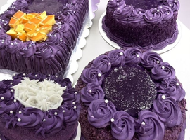 Four purple frosted cakes, including one rectangular cake with orange topping and one round cake with white shreds.