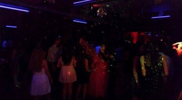 People dancing in a dark club lit by flashing lights and a disco ball.