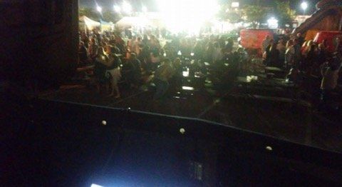 Dark outdoor crowd under bright lights; possibly a concert or festival.