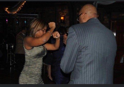 Woman in silver dress dances with man in pinstripe suit at a dimly lit venue.