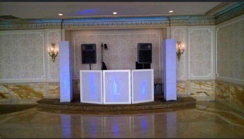 DJ setup on a stage with speakers, a DJ table, and illuminated columns, in a formal ballroom.