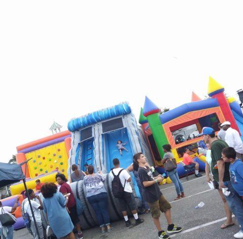 Festival with inflatable slides and climbing wall; people standing around.