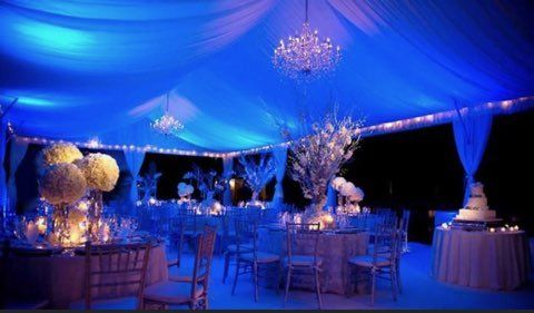 Elegant wedding reception tent lit with blue lights and chandeliers. Tables set for dinner.