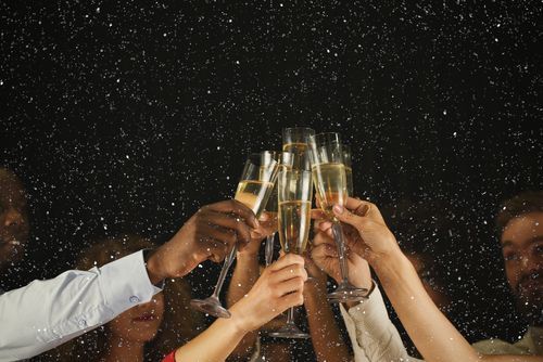 People toasting with champagne flutes against a dark backdrop with confetti.