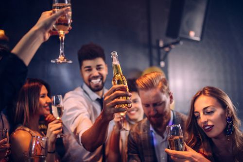 People in a bar, toasting with champagne and beer. Smiling faces, dim lighting, celebratory mood.