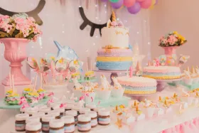 Unicorn-themed dessert table with cake, cupcakes, and treats in pastel colors.