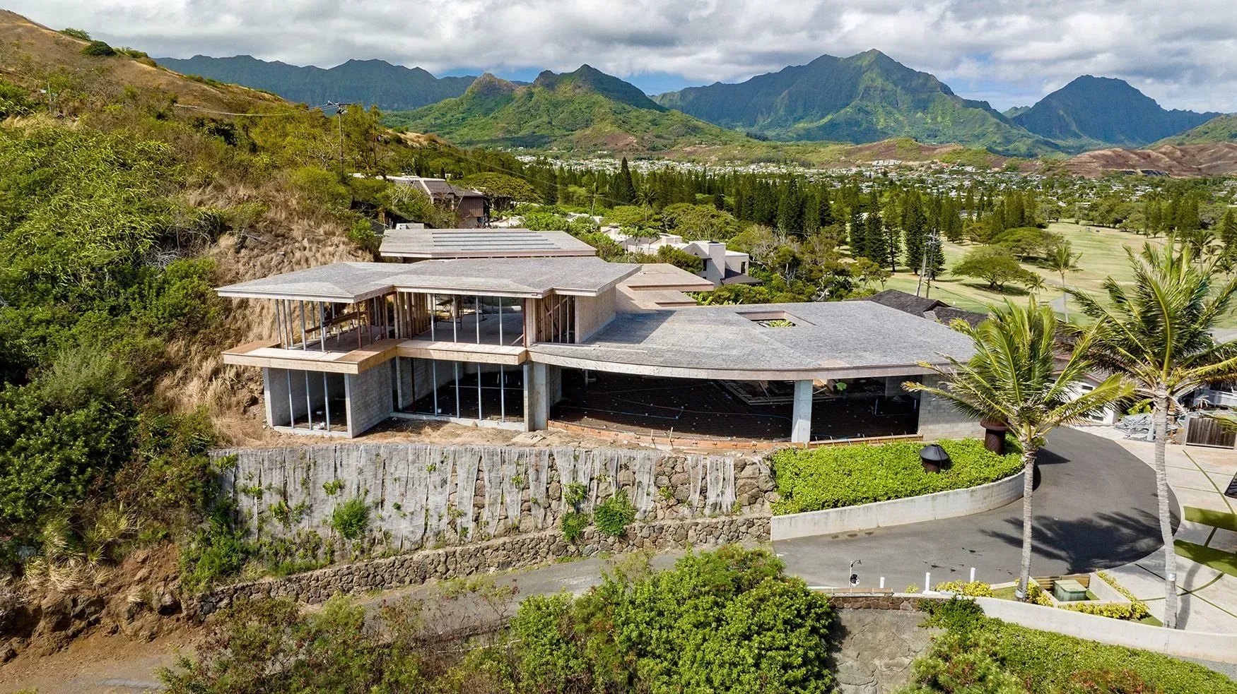 Large modern house on a hillside, overlooking a golf course, with mountain backdrop.