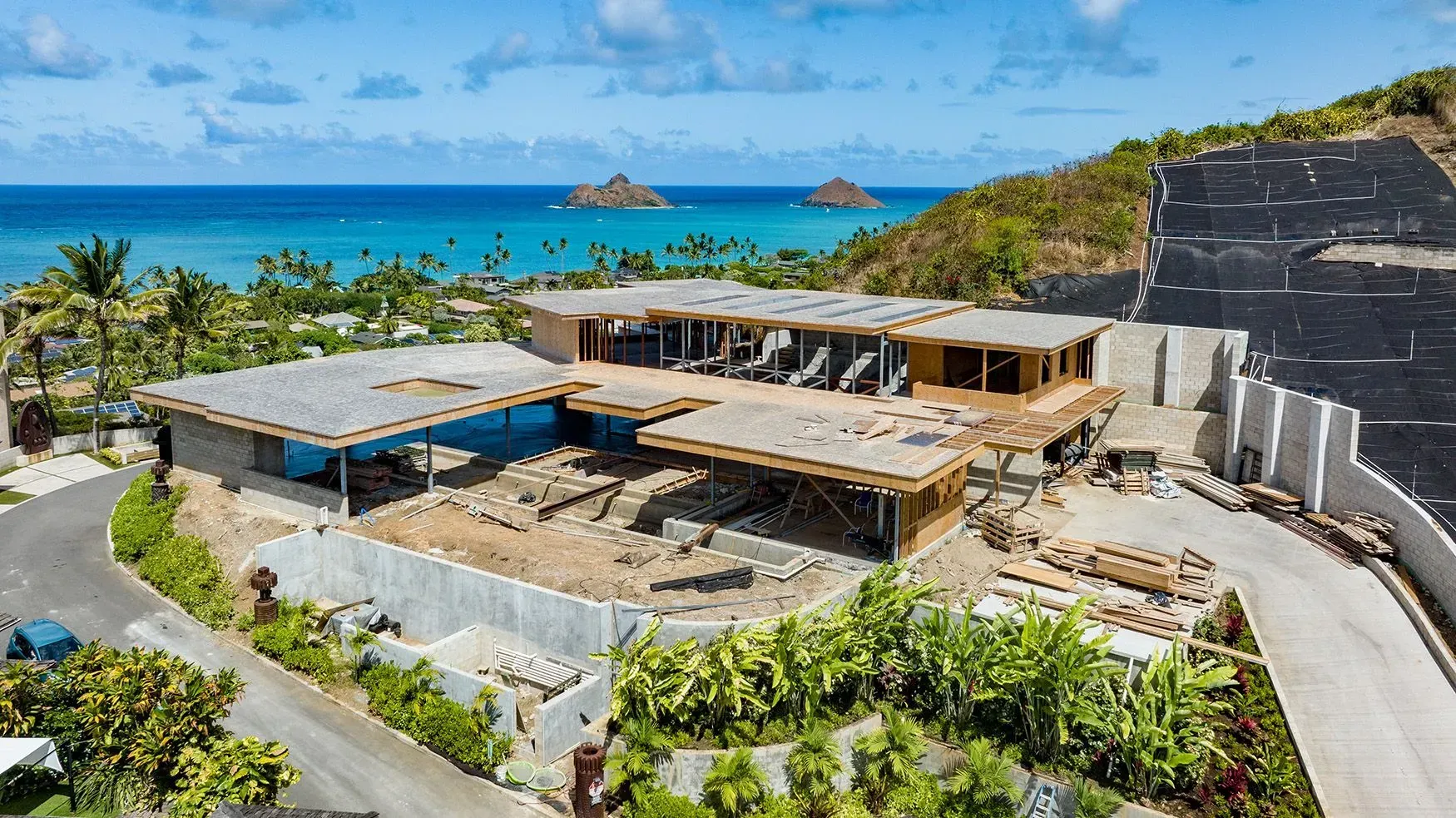 Aerial view of a modern home under construction on a hillside overlooking the ocean.