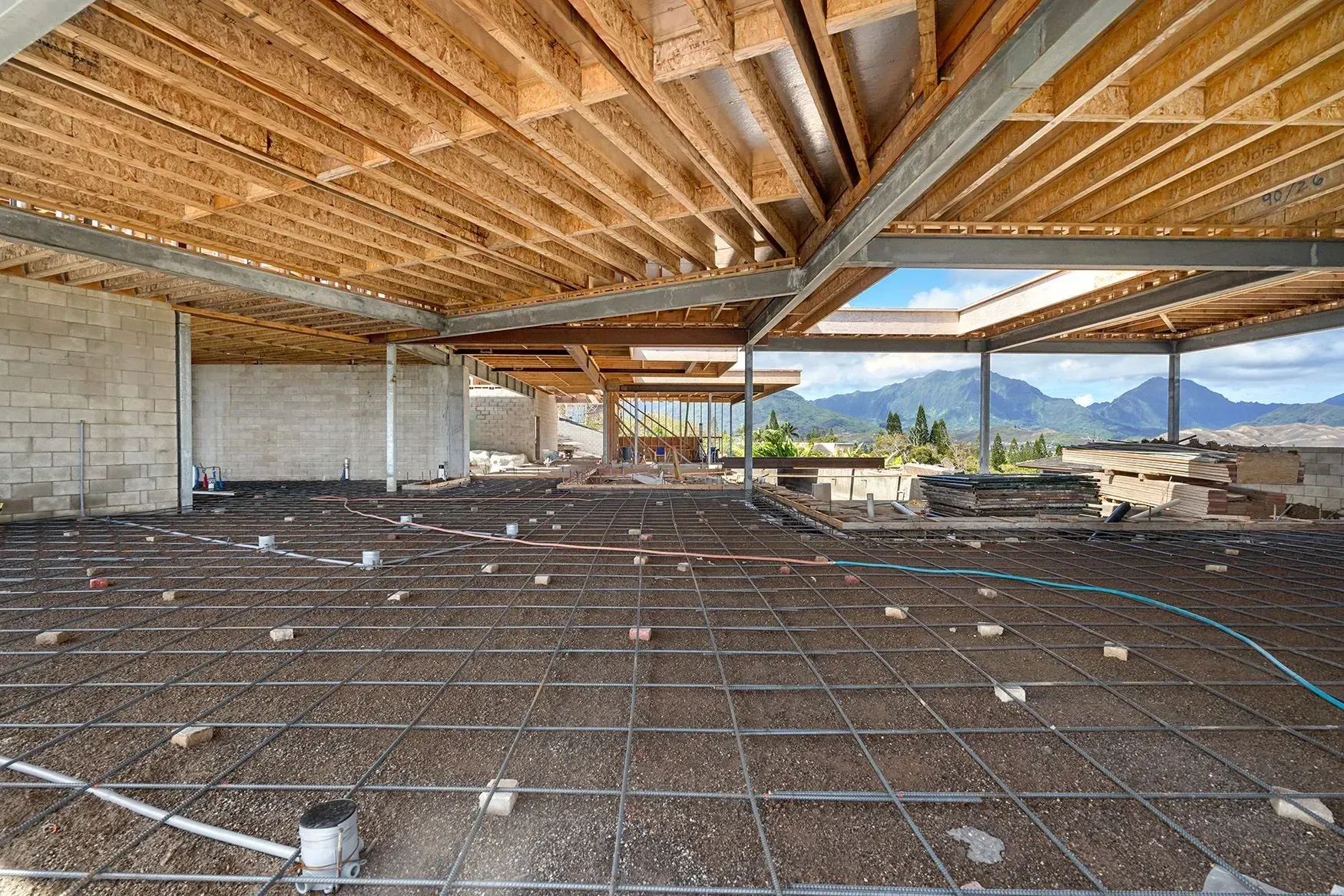 Interior of a building under construction. Exposed wood beams, metal supports, rebar, and mountains visible through openings.