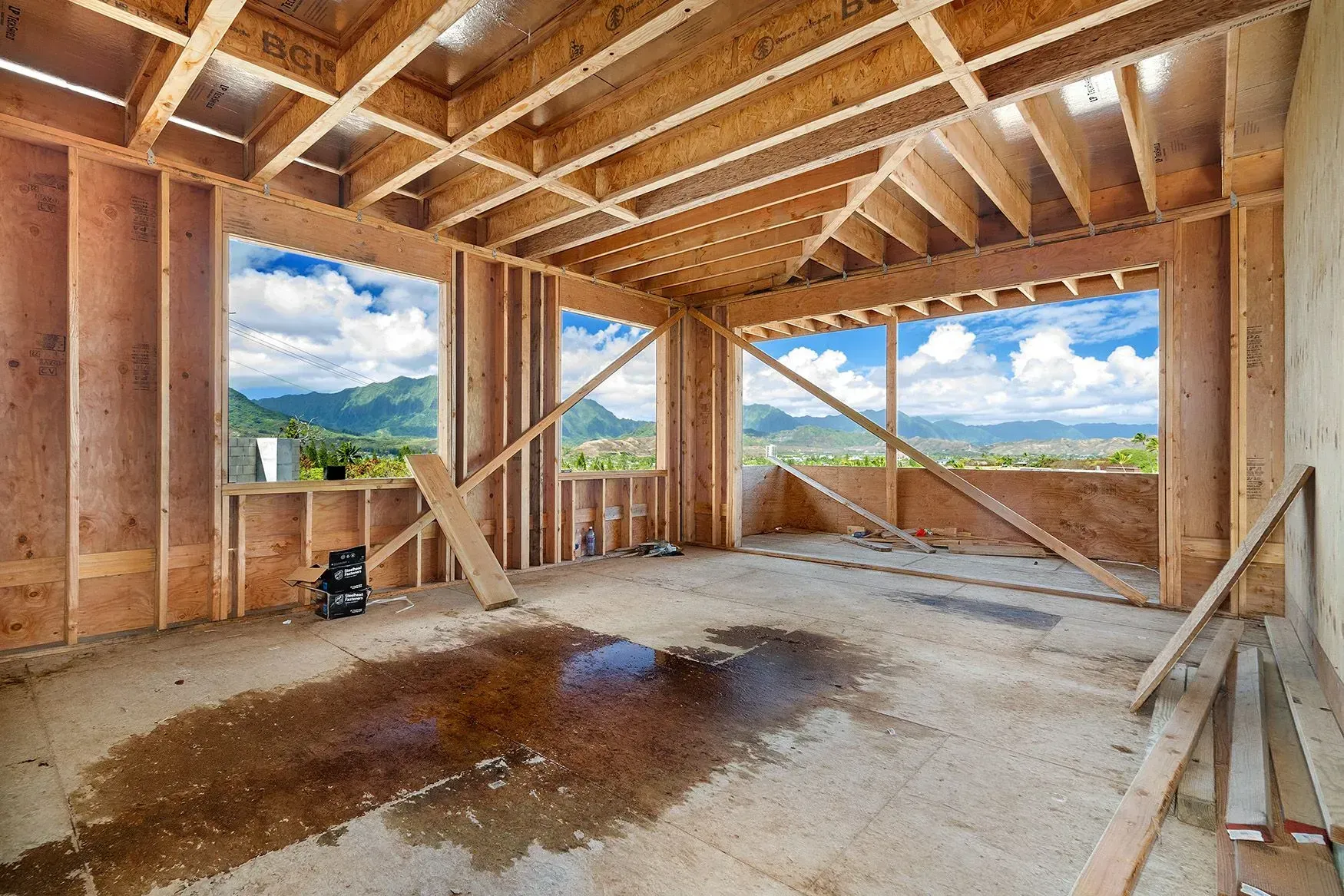 Interior of a building under construction; wooden framing, exposed concrete floor, windows with mountain view.
