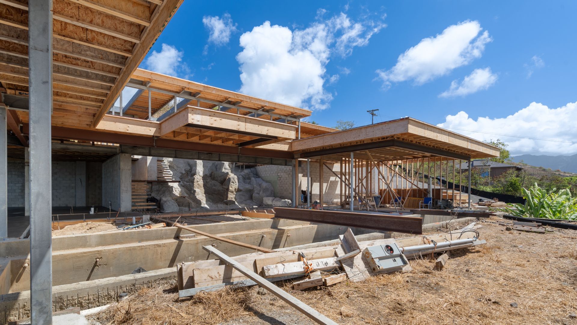 Construction site with wooden framework and concrete foundation against a blue sky.