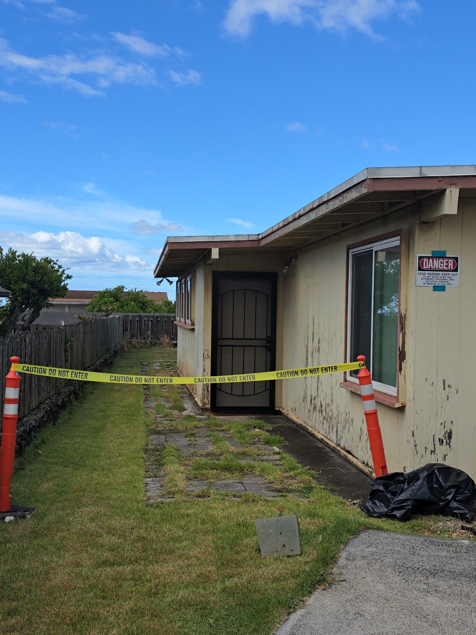 Exterior of a building with a ladder, tarp, and window. Overcast sky.