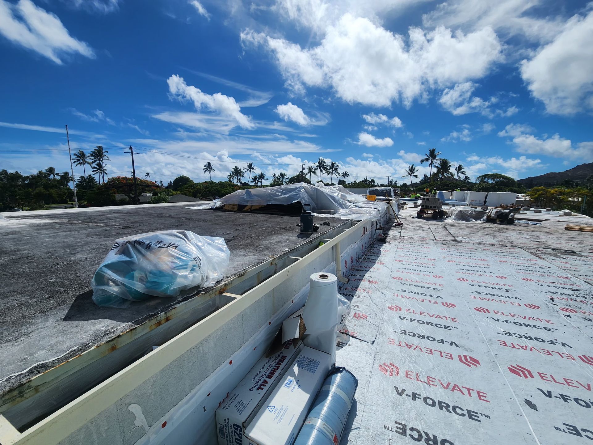 Roof partially covered with white membrane under a partly cloudy blue sky.