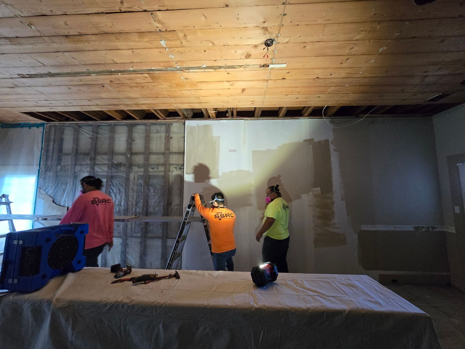 Three workers in a room with exposed ceiling and walls, working on a renovation project.