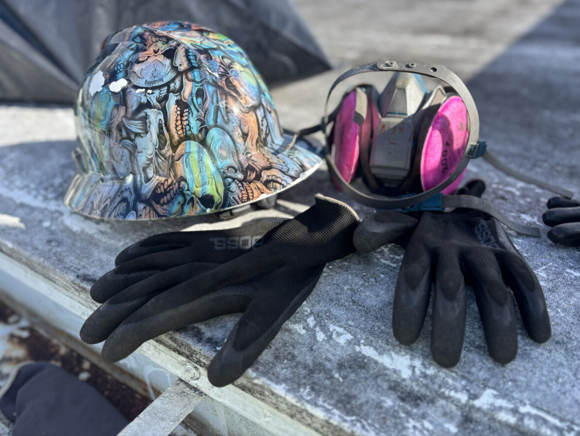 Work safety gear on a rooftop: hard hat, respirator, and gloves.