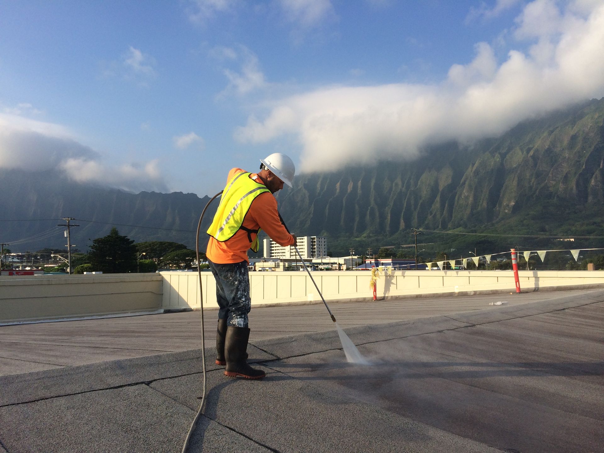 Man power washing a concrete surface on a rooftop, mountains in background, sunny day.