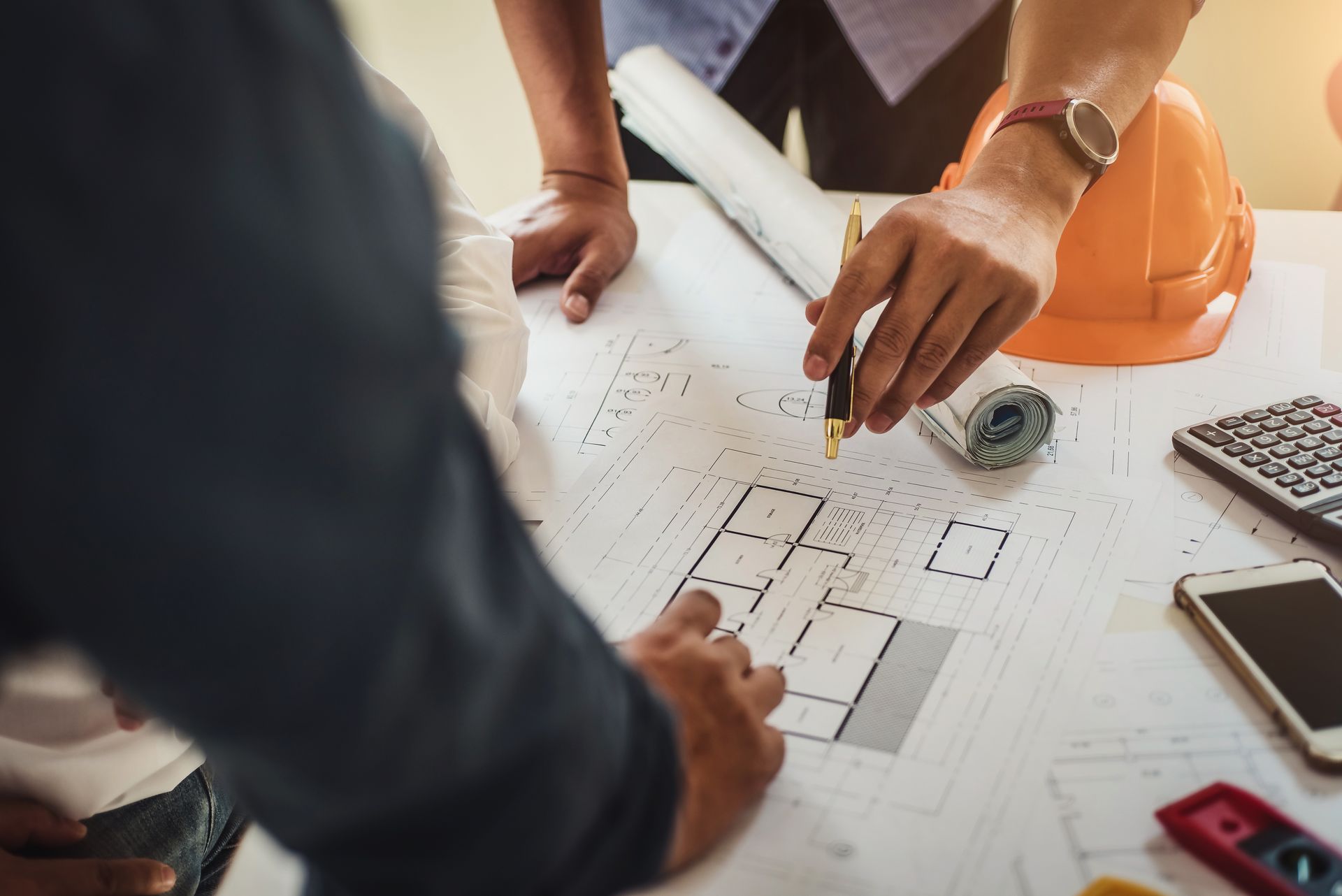 Contractors reviewing construction blueprints with a hard hat, calculator, and pen on a work desk