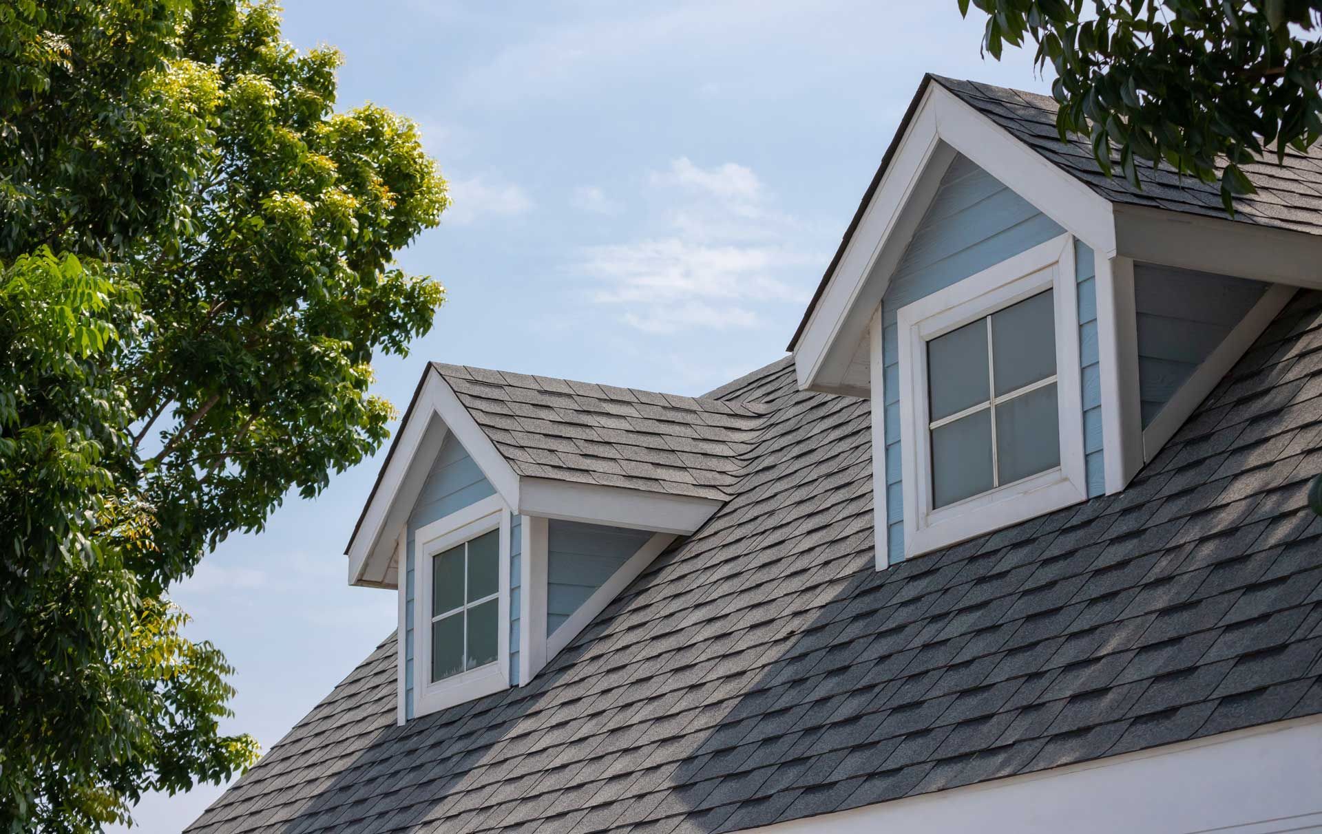 Light blue dormers with white trim on a gray shingled roof under a partly cloudy sky. Light blue dormers with white trim on a gray shingled roof under a partly cloudy sky.