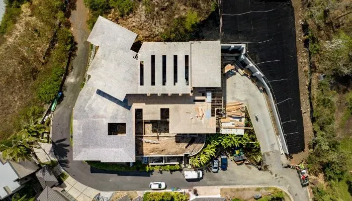 Aerial view of a modern house under construction with a driveway, trees, and parked vehicles.