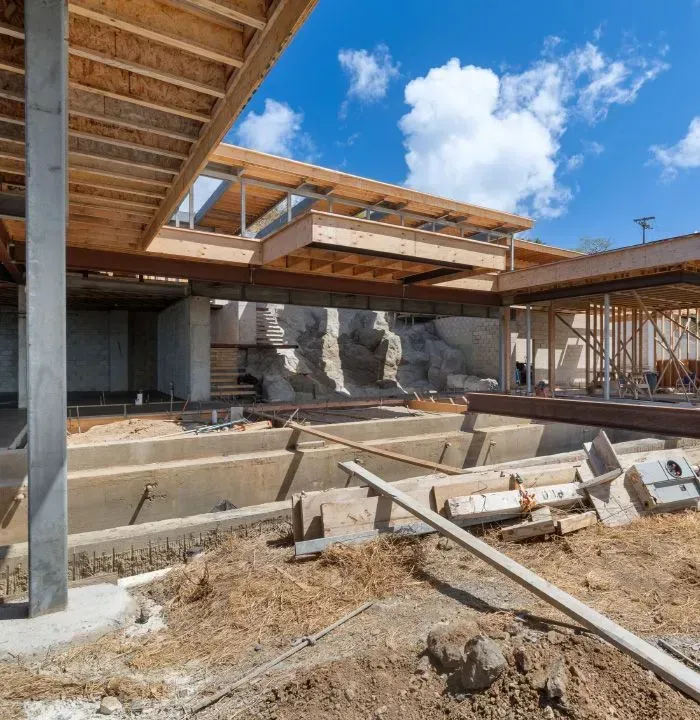 Construction site: framed building with exposed wood beams and concrete foundations against a blue sky.