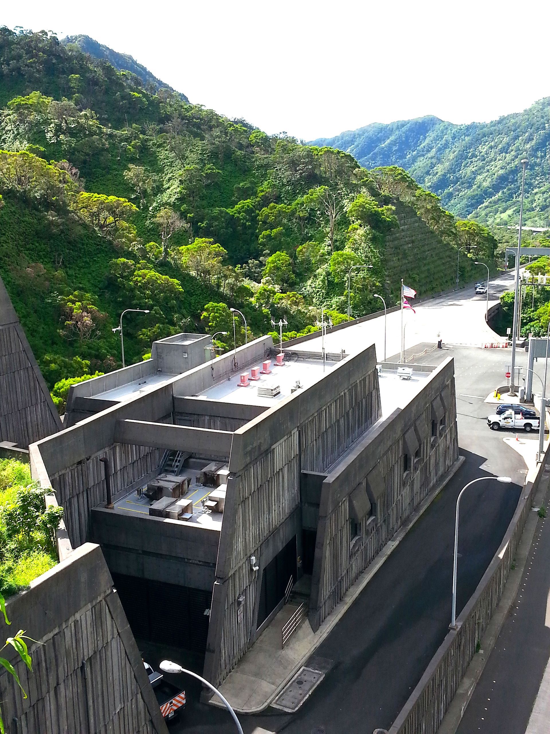 Tunnel entrance with concrete exterior, set against a backdrop of lush green mountains under a bright sky.