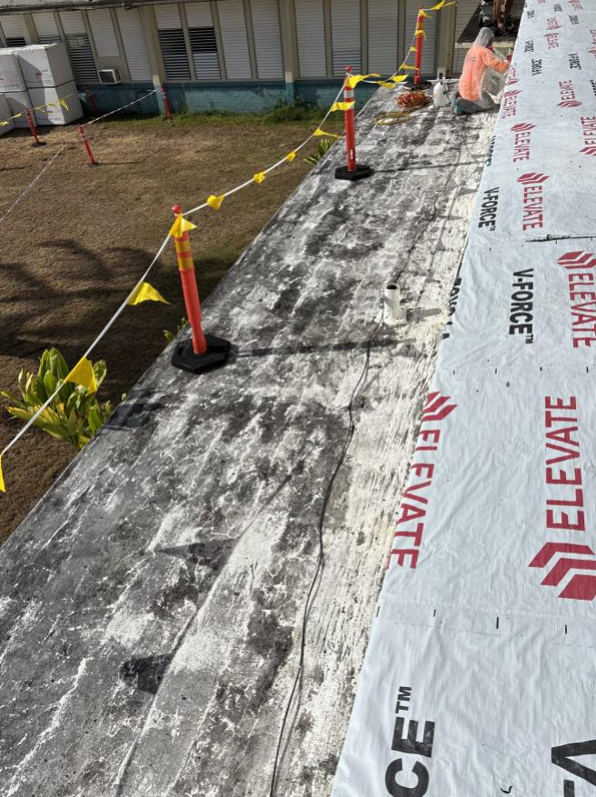 Roofer working on a building roof. Safety barriers, white and gray roof, rolls of white material.