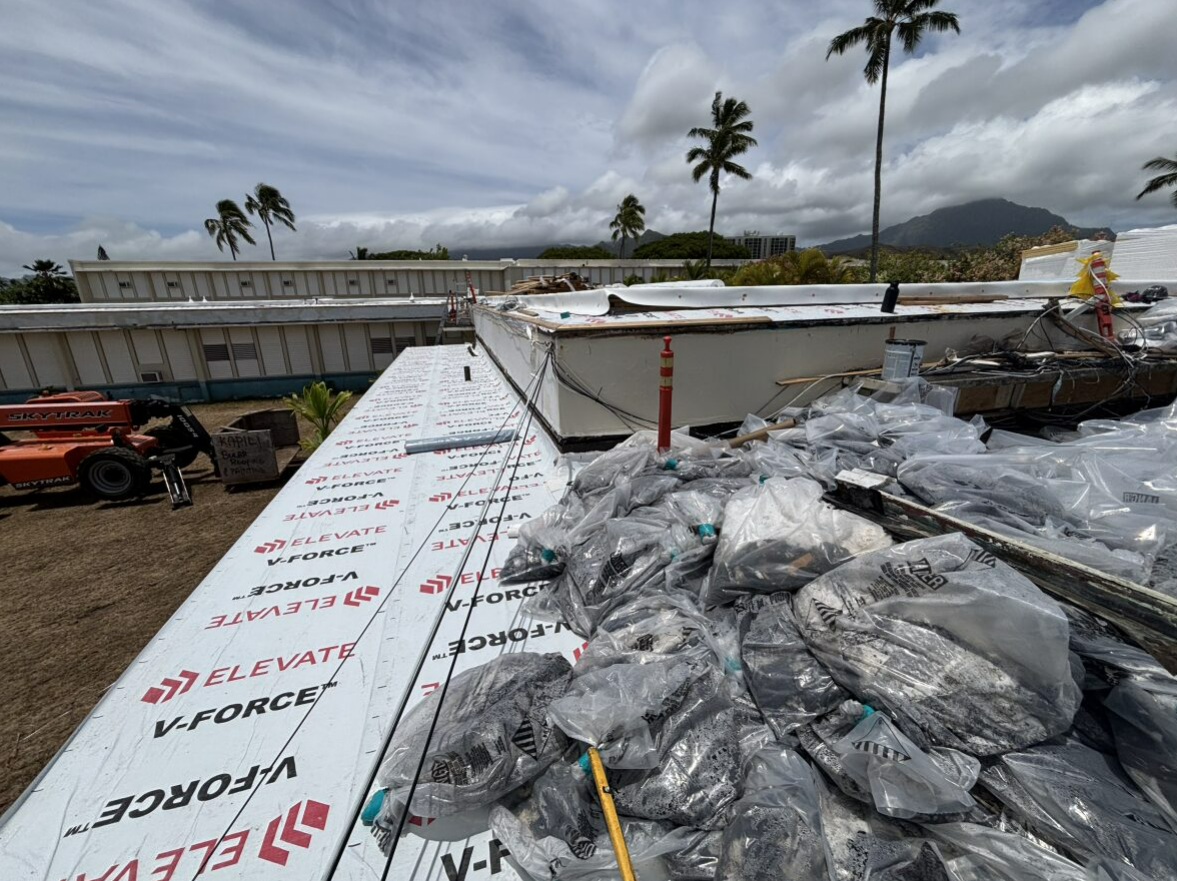 Roofing materials and debris on a partially completed roof. Palm trees and buildings in the background.