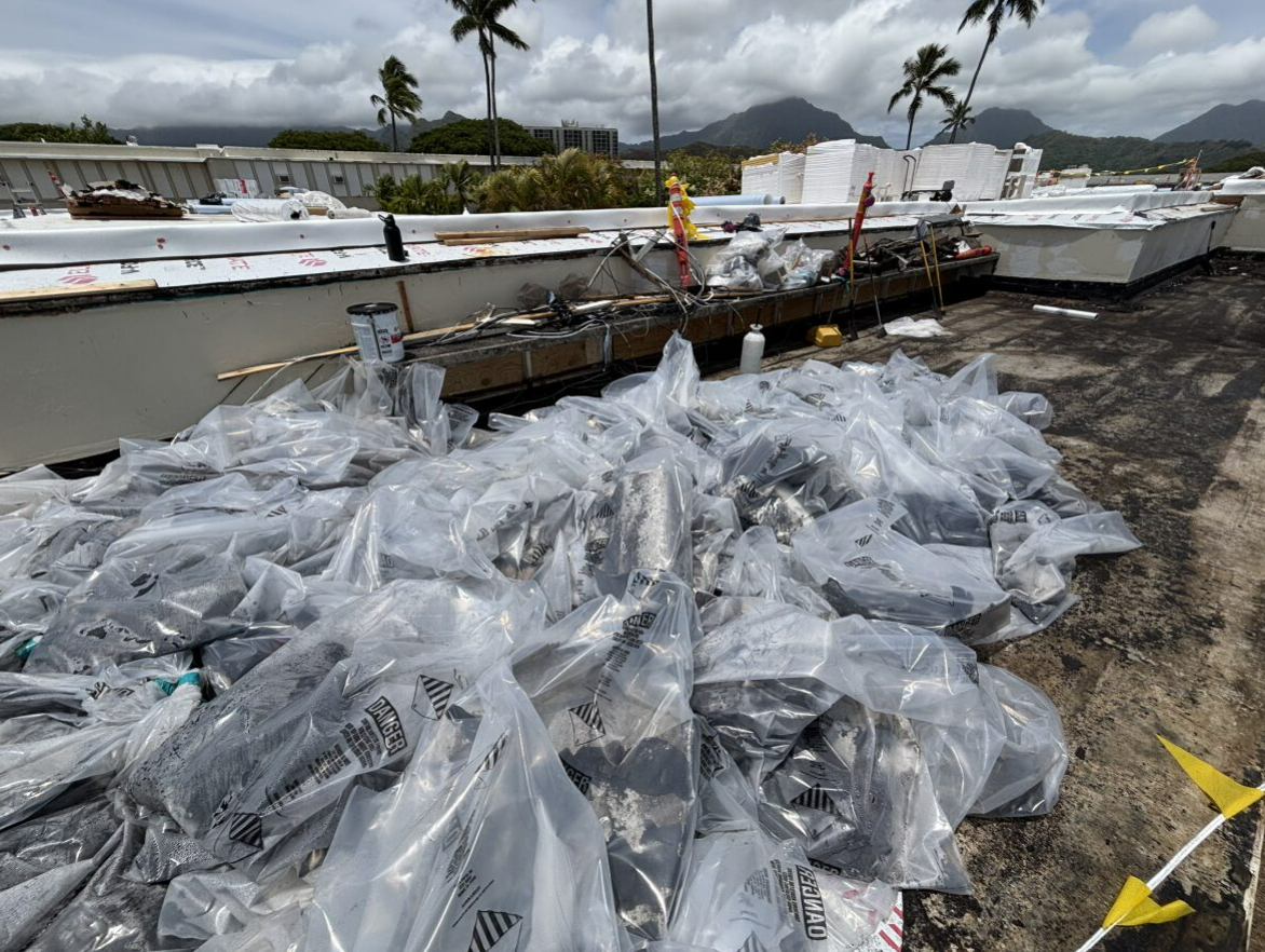 Bags of debris on a flat rooftop. Palm trees and mountains visible in the background, a sunny day.