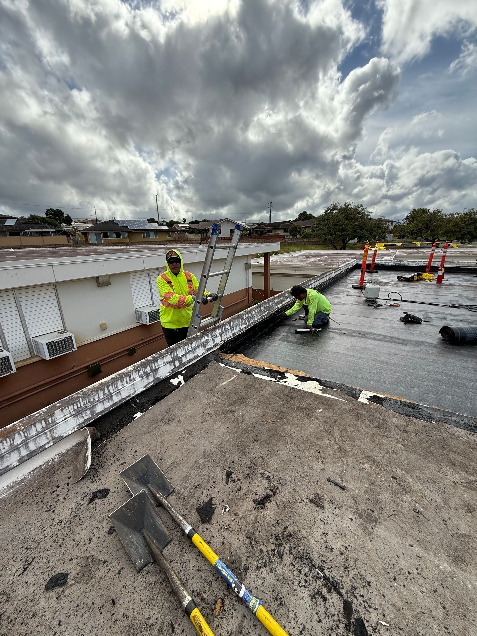 Two construction workers on a rooftop, repairing the surface under a cloudy sky.