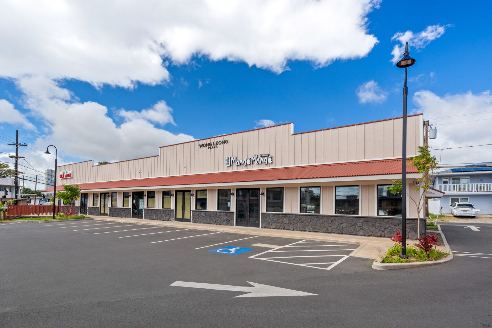 Commercial building with multiple storefronts, blue sky, parking spaces, and handicap parking symbol.