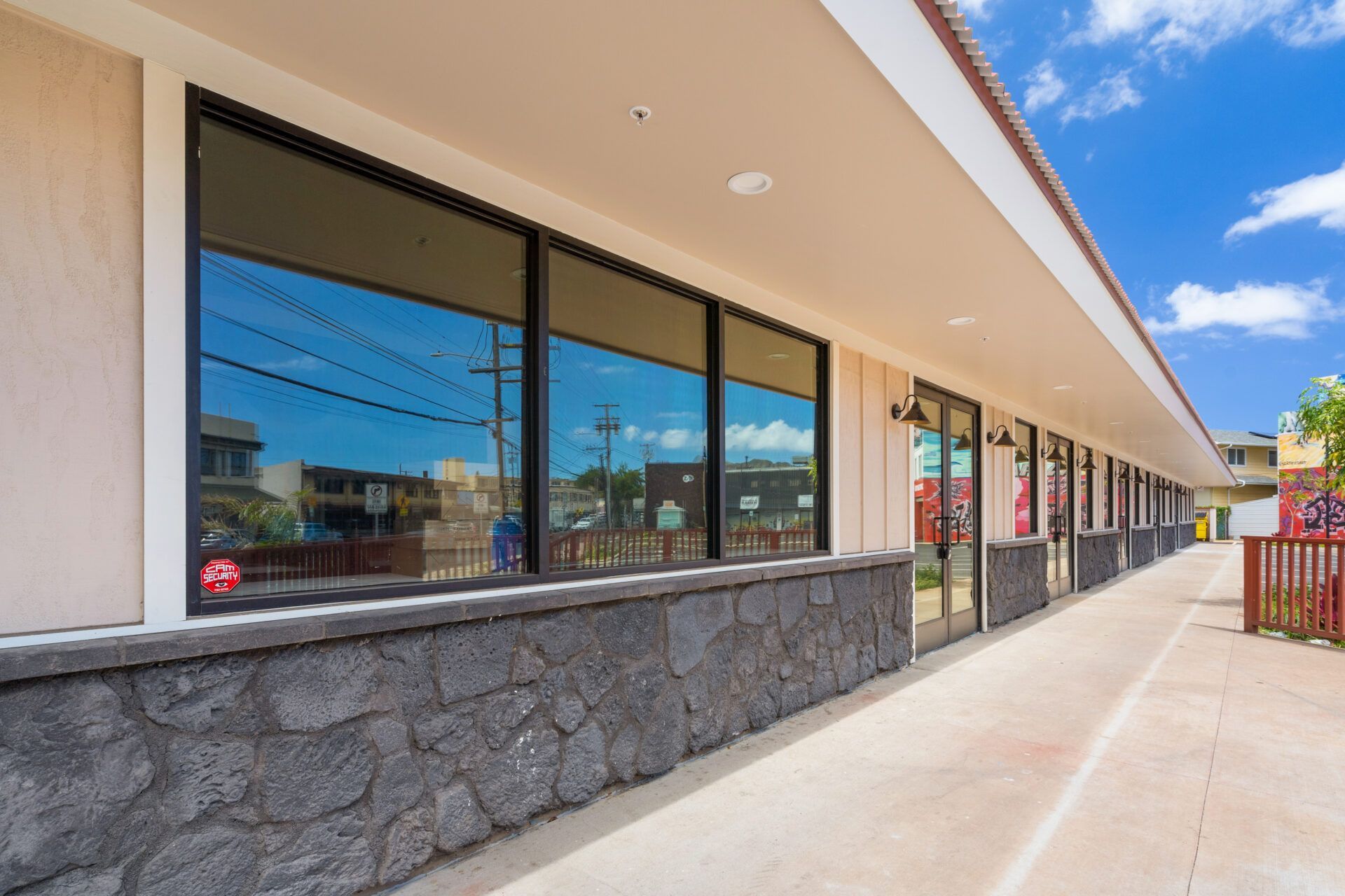 A storefront with large windows, reflecting the sky and street. Beige walls, black stone base.