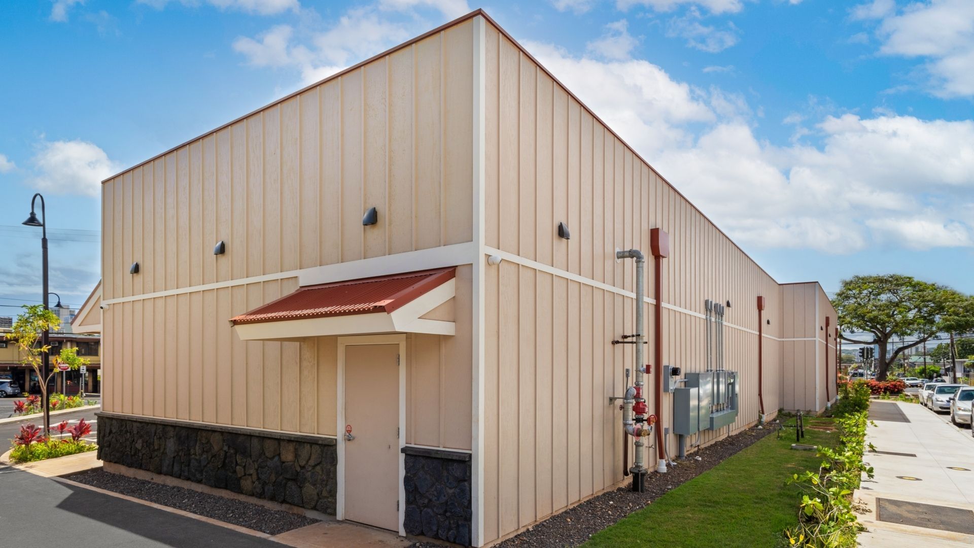 Tan building with a red awning and accents, set against a blue sky with a sidewalk and street view.