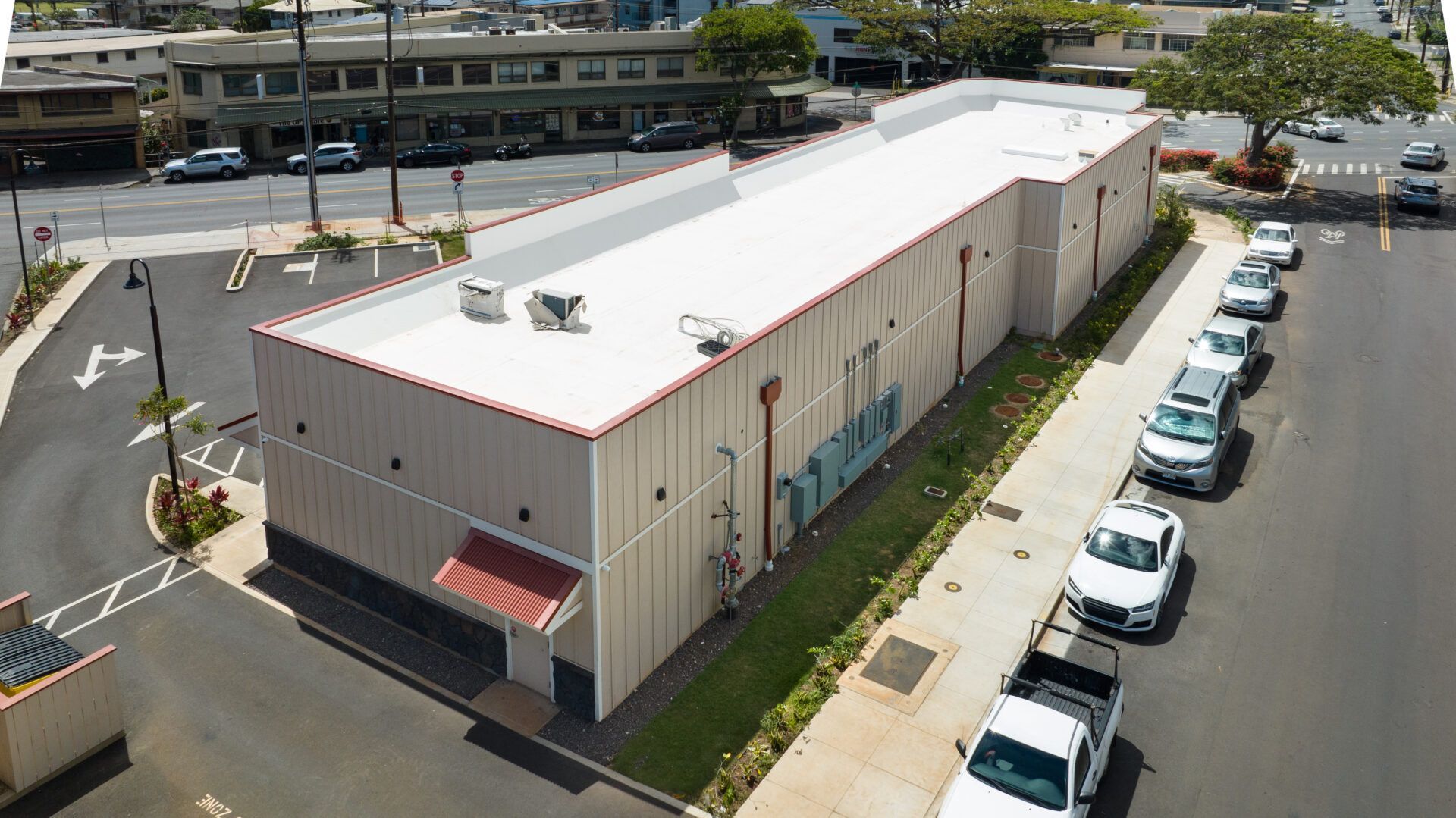 Exterior view of a long, light-colored commercial building with parked cars along the side.