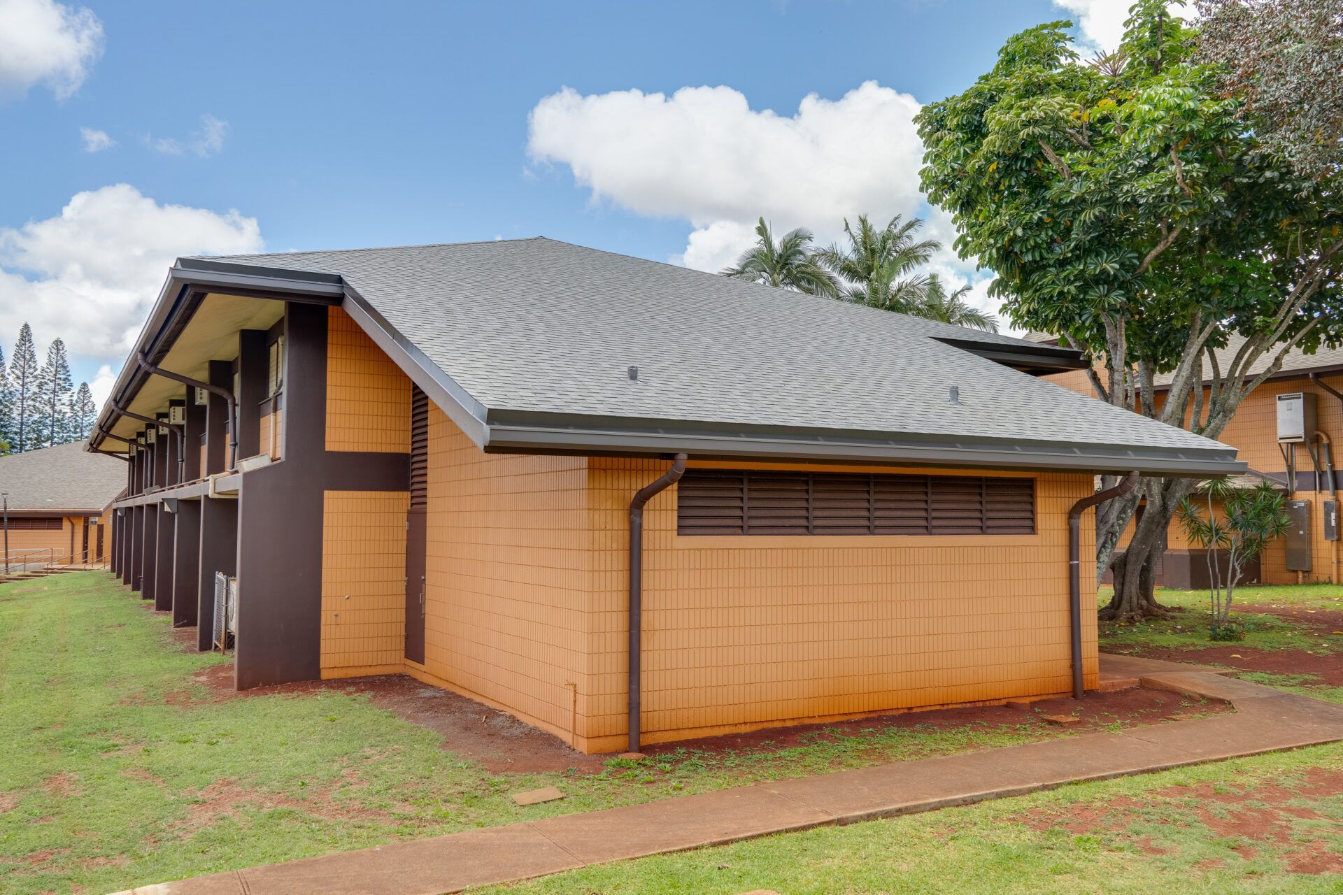 Low-rise brick building with dark roof, brown trim, and grass lawn under a partly cloudy sky.