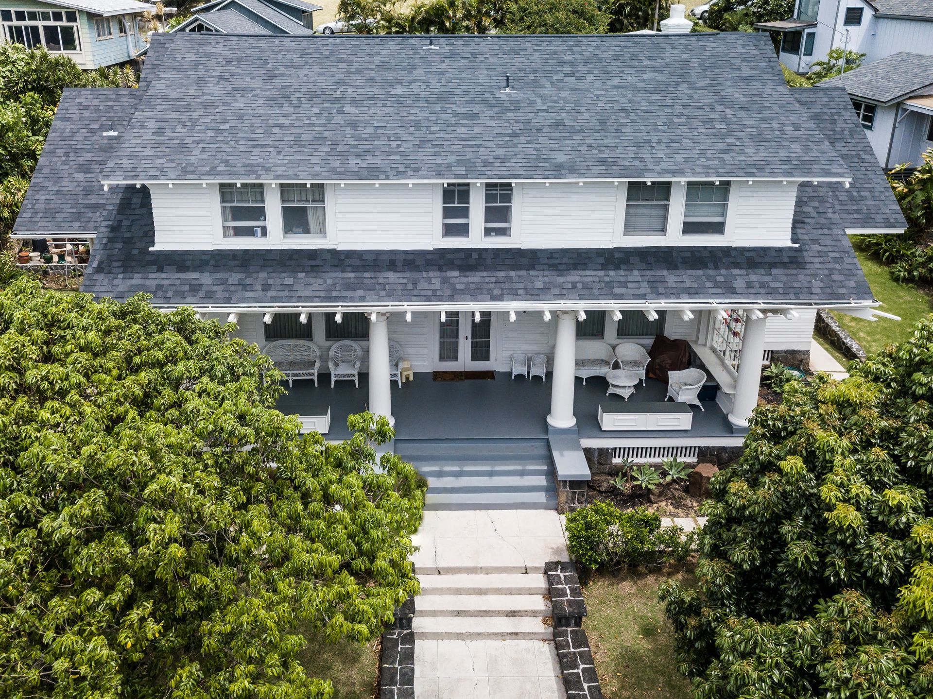 White two-story house with gray roof, front porch, and steps leading to entrance, surrounded by greenery.