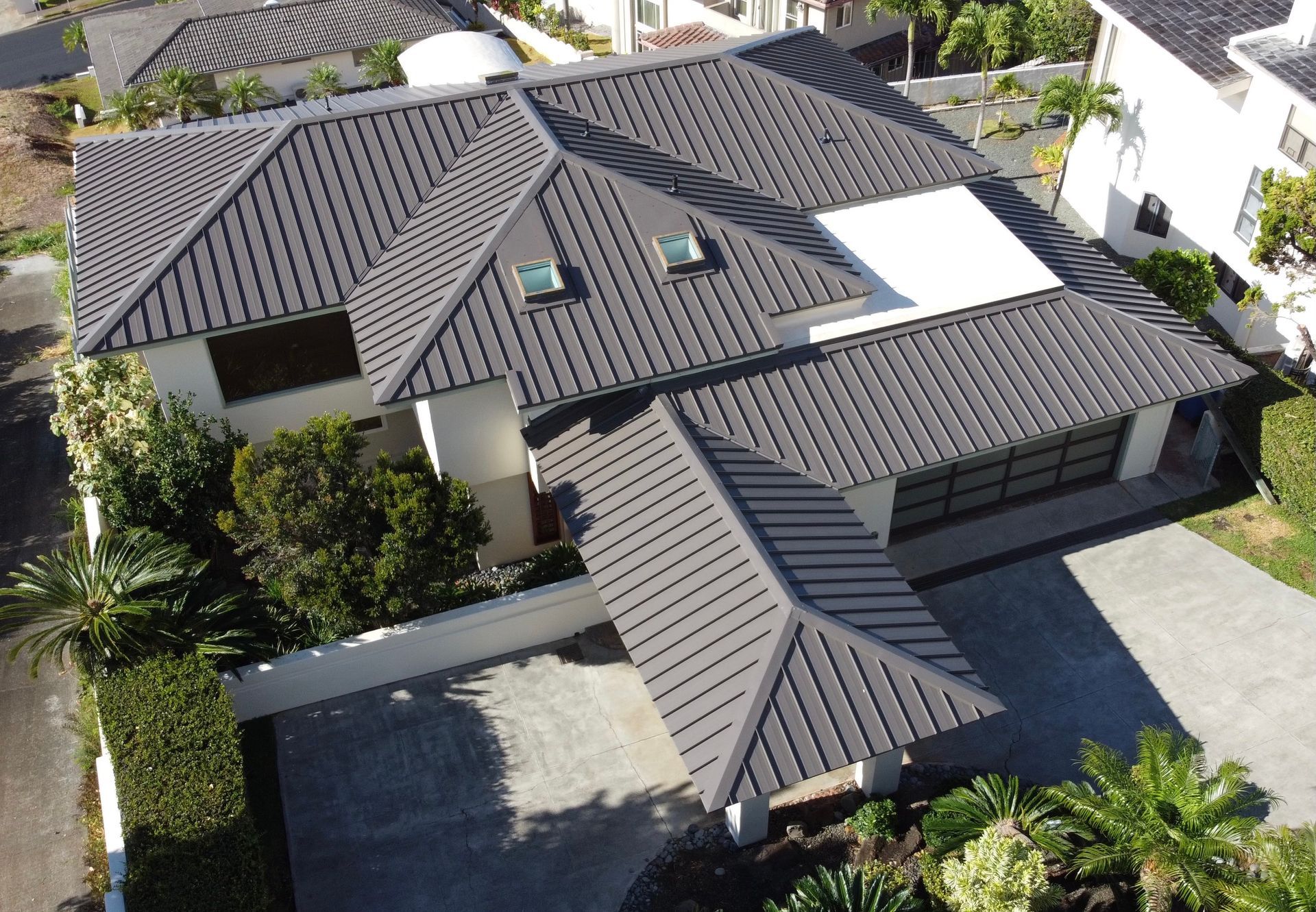 Gray tiled roof of a two-story modern house with a carport and driveway, surrounded by greenery.